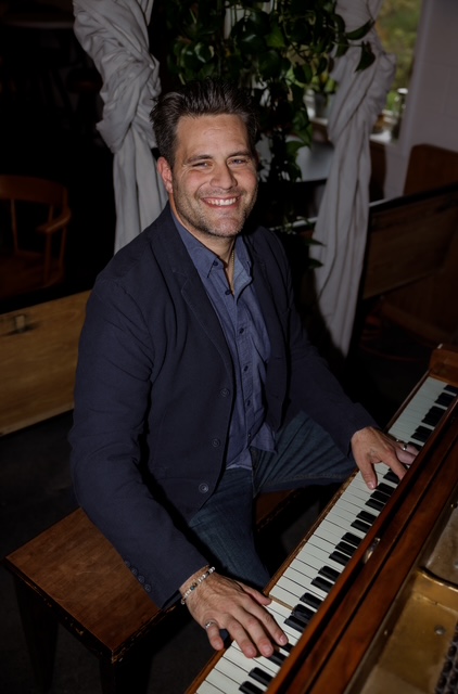 Curtis McLeod smiling at the piano in a monochrome portrait
