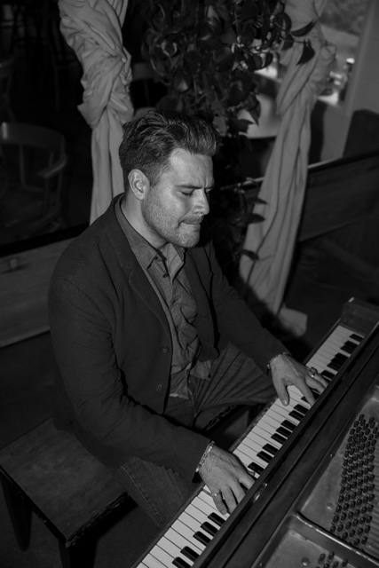 Curtis McLeod seated by the piano in a black and white portrait
