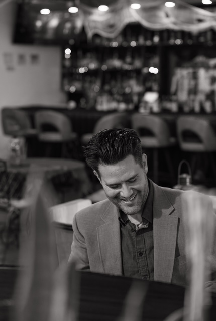 Curtis McLeod standing beside the piano with a refined smile