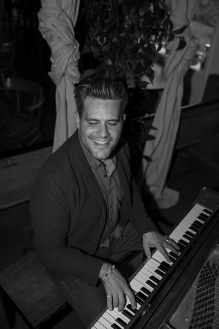 Curtis McLeod smiling while seated at the piano in a lounge